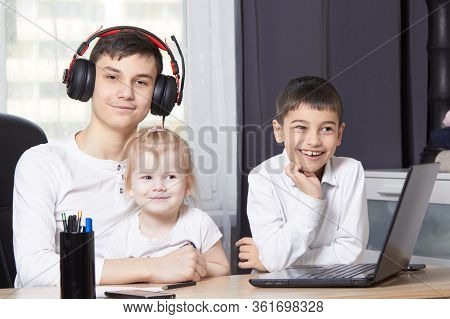 Teenager Looks At A Laptop And Writes Down A Task And Children Interfere With Learning