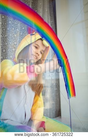 Child Girl In Kigurumi Unicorn Draws The Rainbow On The Window. Stay Home. Flashmob Chasetherainbow.