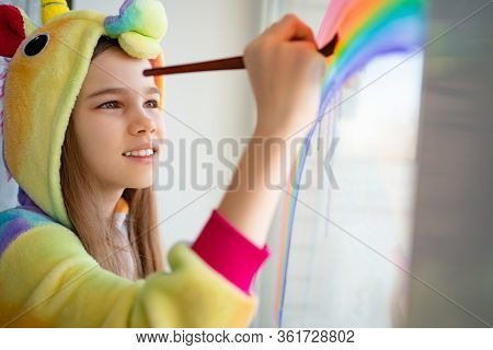 Stay Home. Teen In Kigurumi Unicorn Draws The Rainbow On The Window. Flashmob Chasetherainbow.