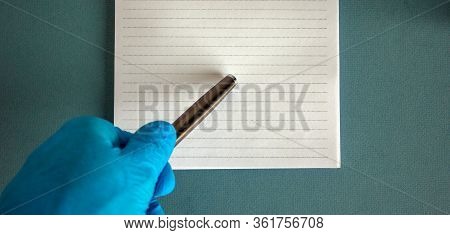 Hand In Blue Glove With Pen And Note On Blue Background.