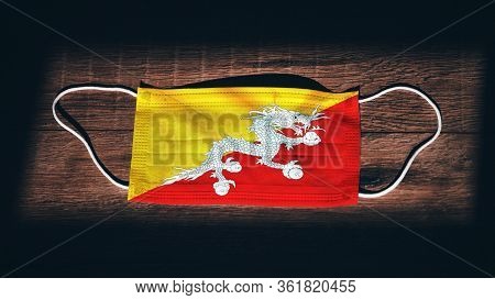 Bhutan National Flag At Medical, Surgical, Protection Mask On Black Wooden Background. Coronavirus C