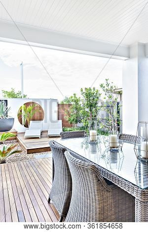 Outdoor Patio Area With Rattan Chairs On The Wooden Floor Next To The Glass Panel Table, There Are C