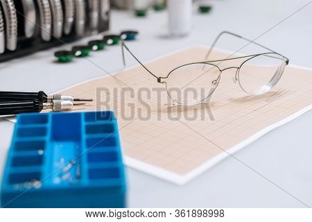 Optician Repairing Equipment And Fixing Eyeglasses. Broken Glasses Laying On Table In Optician Works