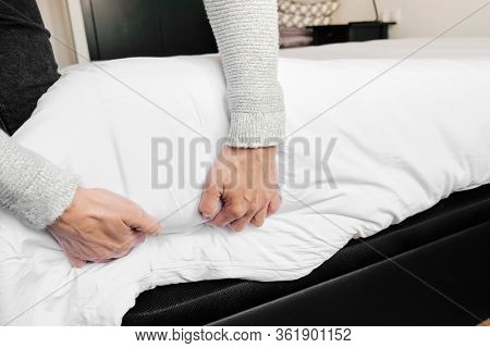 closeup of a young caucasian man making the bed with white bedsheets