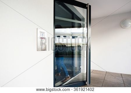 Woman Silhouette Entering Glass Door In Modern Apartment Building With Modern Steel Interphone Inter