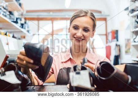 Woman shoemaker taking shoes to be repaired off the shelf in her workshop