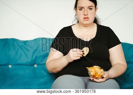 Overeating And Gluttony Concept. Mindless Snacking, Home Sedentary Lifestyle. Obese Woman Sitting On