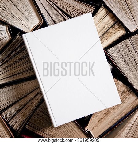 Mockup Of Closed Blank Square Book Rests On Open Old Multicolored Books