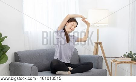 Beautiful Asian woman stretches out her arms on her favorite sofa in the living room, Body and mind 