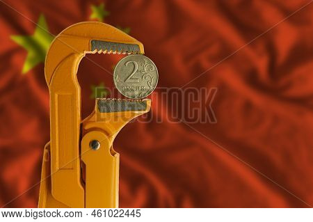 Russian Two Rubles Coin Held In An Orange Plumber Wrench On The Background Of The Flag Of China. Rev