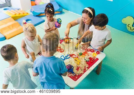 Fun Sensory Play With Moldable Kinetic Sand At Nursery School. Toddlers Standing Around The Table An