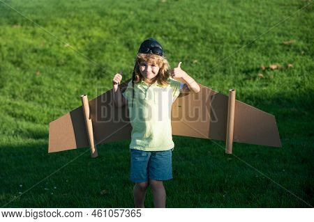 Child Boy Like A Pilot With Toy Wings Against Green Grass. Kids Freedom Concept. Dreams Of Becoming 