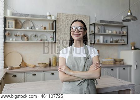 Portrait Of A Young Beautiful Woman Cook, Confectioner. She Is Standing In A Beige Apron And Glasses