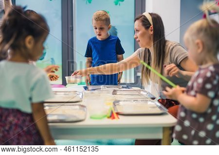 Sensory Play At Multi-cultural Nursery School. Toddlers With Their Teacher Playing With Striped Stra
