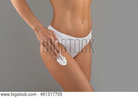 Unrecognizable Slim Woman In White Panties Applying Moisturising Body Cream On Legs