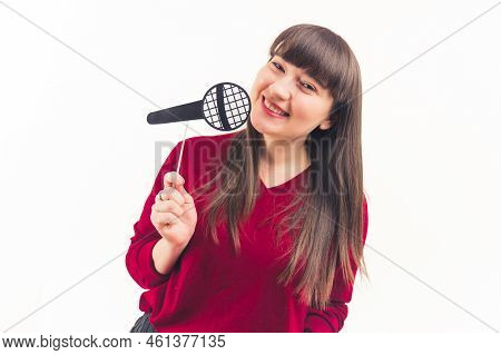 Young Caucasian Brunette Woman With Bangs Smiling Holding Fake Paper Microhone. Studio Shot. Isolate