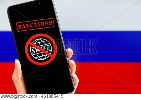 Ukraine, Kiev - February, 23 2022: Hand Holding Mobile With Crossed Out Swift Logo And Russian Flag 