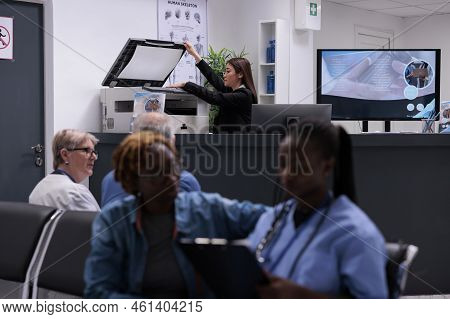 Female Secretary Working With Copy Printer At Hopital Reception Desk To Do Medical Reports And Regst