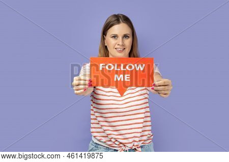Portrait Of Joyful Beautiful Blond Woman Wearing Striped T-shirt Holding Out Red Card With Follow Me