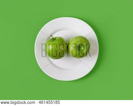 Two Fresh Green Apples On A White Plate Over Green Background. Raw Organic Fruits For Slimming Diet 