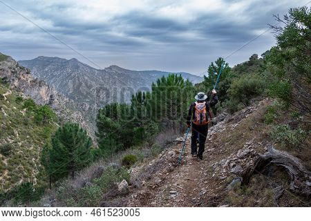 Hiker Walking Along A Path In The Sierra Almijara And Tejeda With Pine Trees And A Stormy Sky