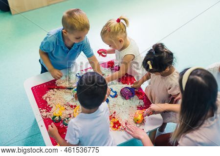 Fun Sensory Play With Moldable Kinetic Sand At Nursery School. Toddlers Standing Around The Table An