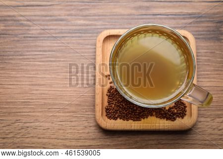 Cup Of Aromatic Buckwheat Tea And Granules On Wooden Table, Top View. Space For Text
