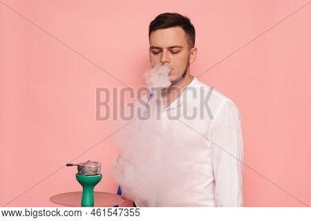 A Male Model Smokes A Hookah, Sheesha And Enjoys It. Pink Background