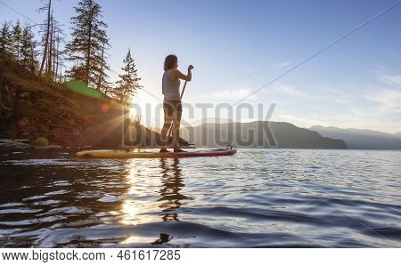 Adventurous Woman Paddling On A Paddle Board In A Peaceful Lake.