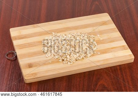 Heap Of The Raw Thick-rolled Oats On The Bamboo Cutting Board On The Red Wooden Table
