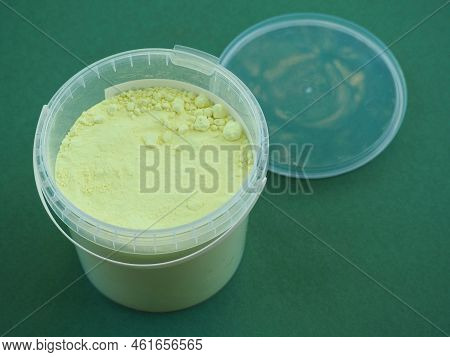 Sulfur Powder In A Plastic Container. Brimstone For Industrial Use. Chemical Substance On A Green Ba