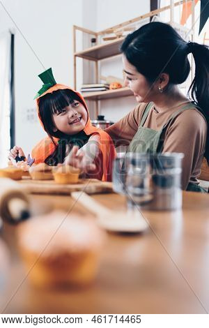 Young Girl And Mother At Halloween Making Treats And Cupcake On Table. Happy Halloween Day
