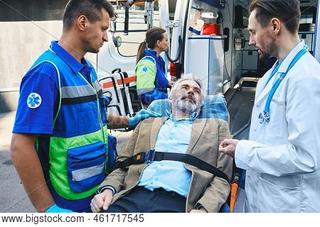 Paramedic And Doctor Examining Of Senior Male Patient Lying In Ambulance Gurney Brought To Hospital 
