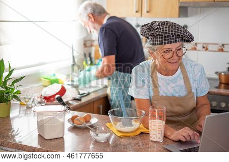 Smiling Senior Woman Browsing By Laptop Looking For A Recipe To Prepare Her Homemade Plumcake While 