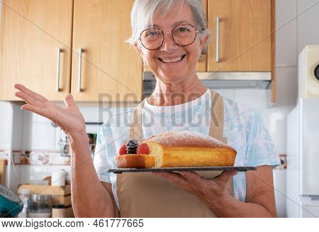 Elderly Caucasian Woman In The Home Kitchen Proudly Displays A Freshly Baked Homemade Plumcake Serve