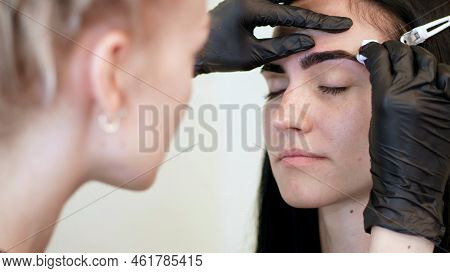 Beauty Saloon. Cosmetologist, In Black Rubber Gloves, Gently Wipes His Eyebrows With A Cotton Disc, 