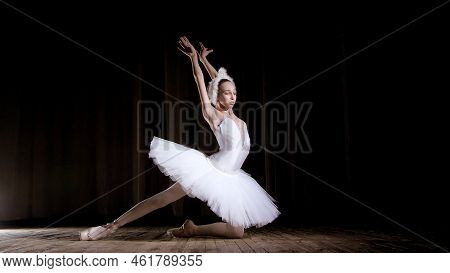 In Rays Of Spotlight, On The Stage Of The Old Theater Hall. Young Ballerina In Suit Of White Swan An