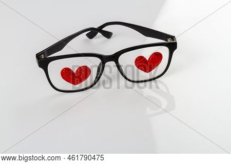 Close Up Glasses With Red Hearts Atteched To Lenses. White Reflective Background.
