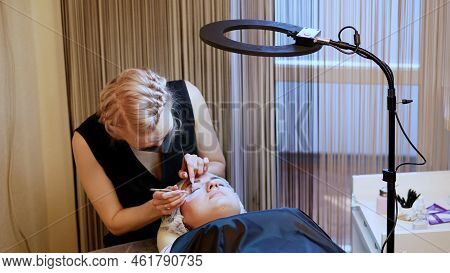 Beauty Saloon. Procedure For Eyelash Extension. The Master In The Bandage On The Face, Glues Each Ci