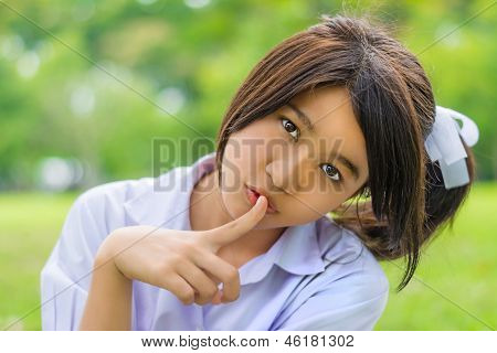 Милые тайские школьница делает жест Hush в Bachground зелеными Боке.