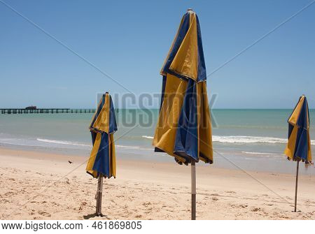 Blue And Gold Folded Umbrellas Stuck In The Sandy Shoreline At Iracema Beach In Fortaleza, Brazil