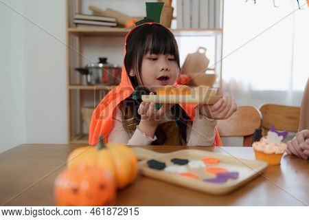 Young Girl And Mother At Halloween Making Treats And Cupcake On Table. Happy Halloween Day