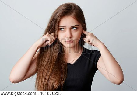Young Annoyed Girl In Black Shirt Sticking Fingers In Ears And Looking Right To The Source Of Irrita