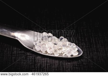 Desiccant Or Silica Gel In White Paper Packaging And Spread On Isolated Black Background, Anti Milde