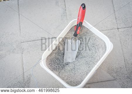 Full Bucket Of Polymeric Paver Sand With Trowel On Top Of Gray Concrete Patio Stone Paver Walkway