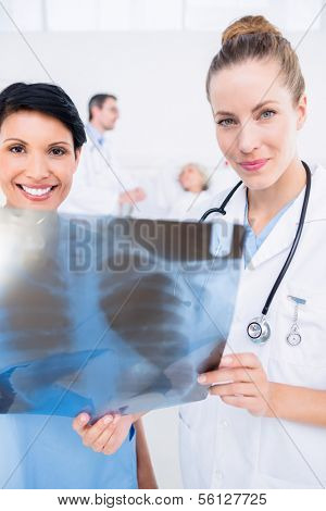 Portrait of a smiling doctor and surgeon examining x-ray with patient in background at the hospital