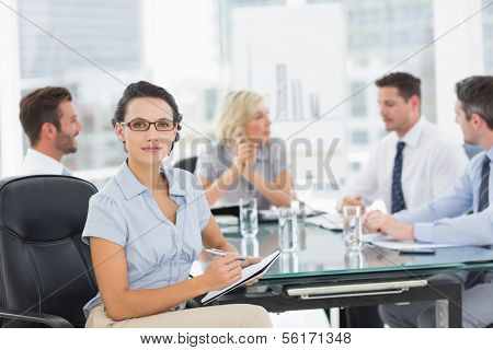 Young businesswoman holding clipboard with colleagues discussing in background at a bright office