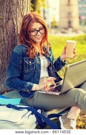 education, technology and internet concept - smiling redhead teenager in eyeglasses with laptop computer and take away coffee or tea