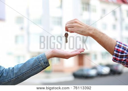 Man and woman hands hold keys near apartment house