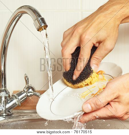 Hands with sponge wash the dirty dishes under running water in kitchen